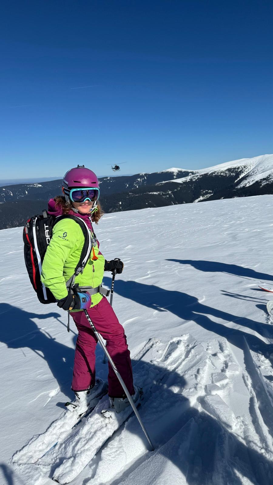 Csilla on skis with a helicopter in the distance
